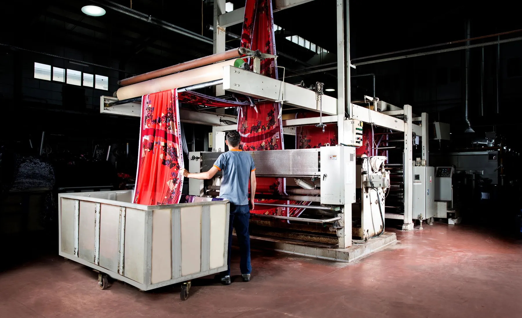 Worker at a textile printing machine feeding a long length of red patterned fabric