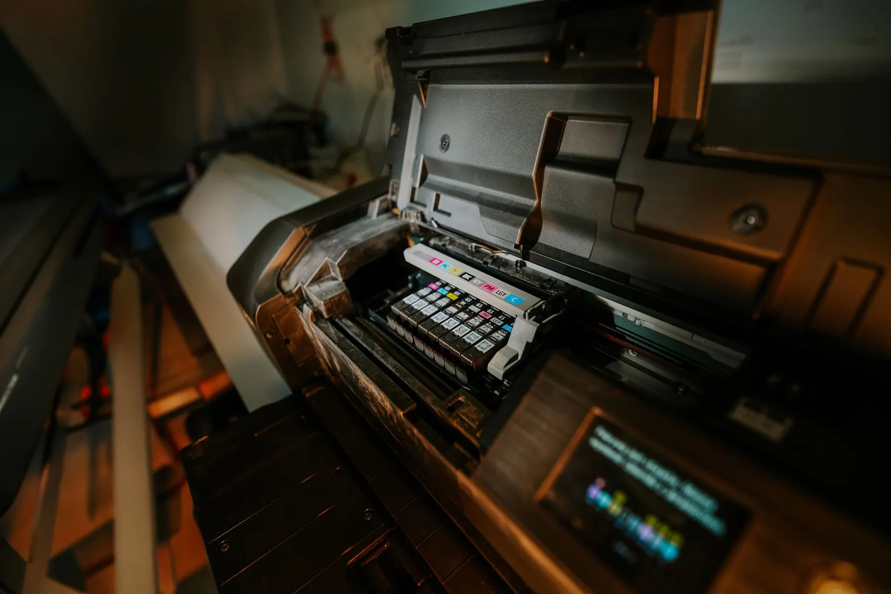 Inside a wide-format printer showing the print head and ink cartridges in warm light