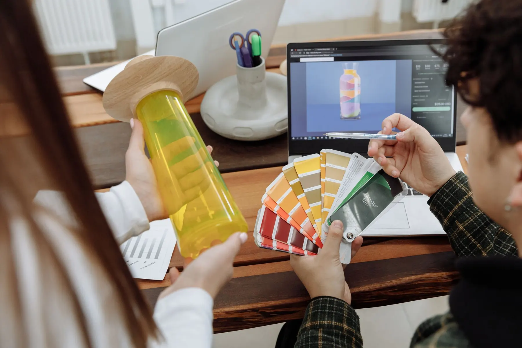 Designers comparing a colour fan against a product mock-up on a laptop
